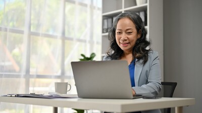 Middle aged asian woman smiling at computer screen