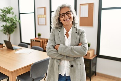 Middle aged woman with grey hair and glasses smiling at the camera with crossed arms.